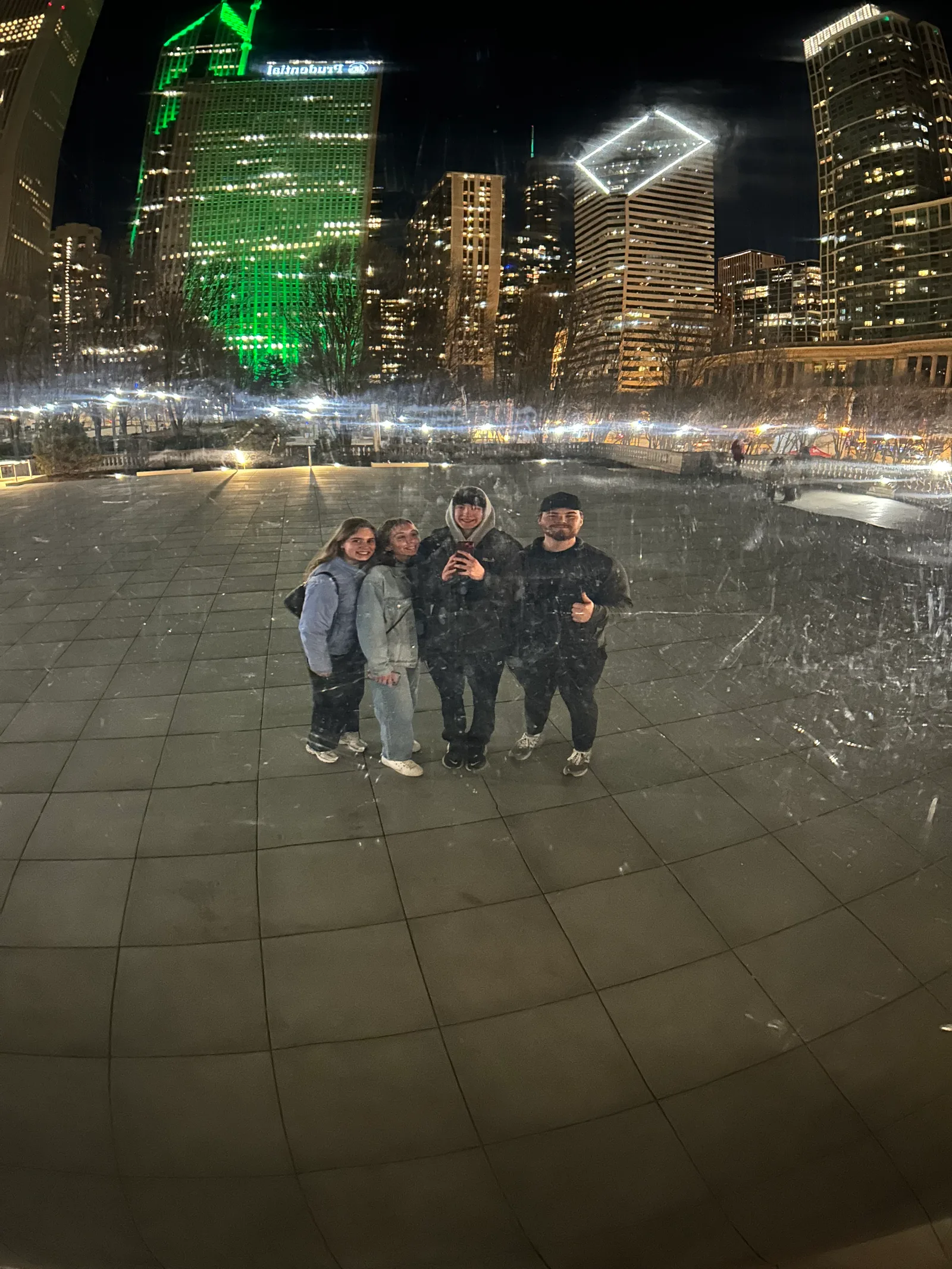 A group reflected in Cloud Gate at night.
