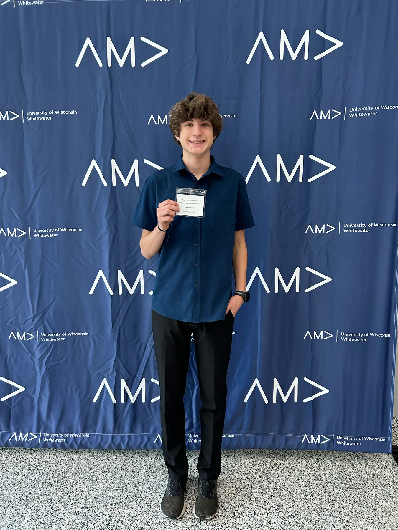 An attendee holding a conference name badge in front of the AMA backdrop.