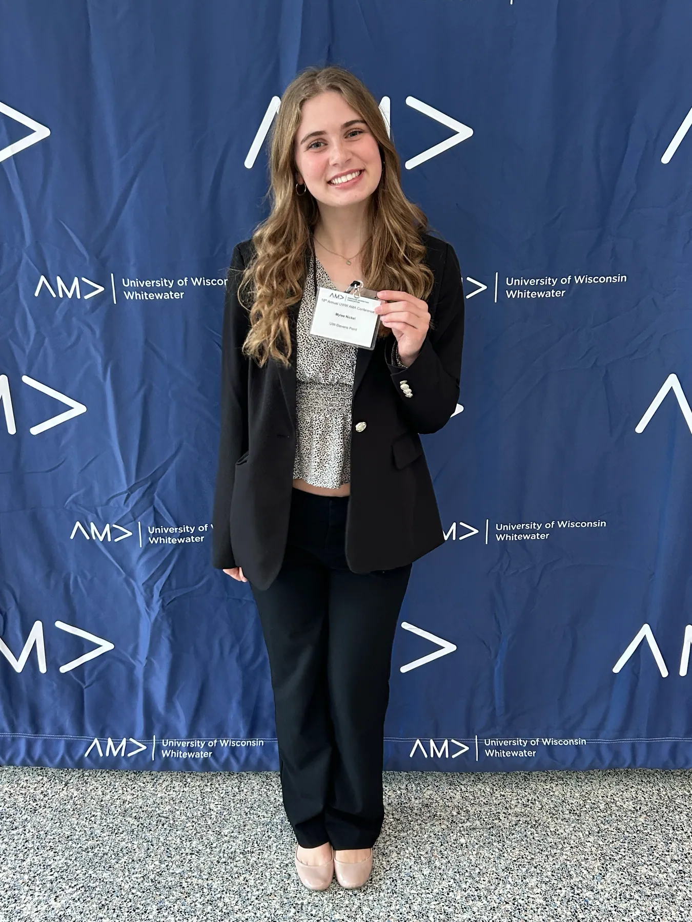 An attendee holding up a conference name badge in front of the AMA backdrop.
