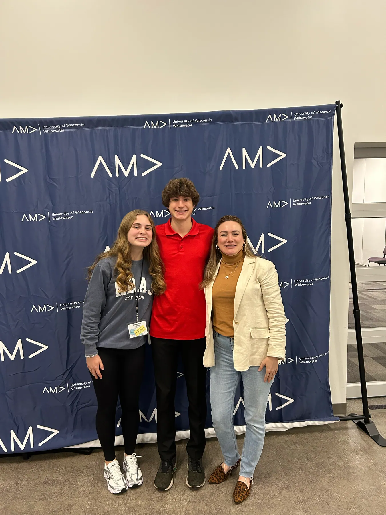 Three attendees in casual clothes in front of the AMA backdrop the evening before the conference.