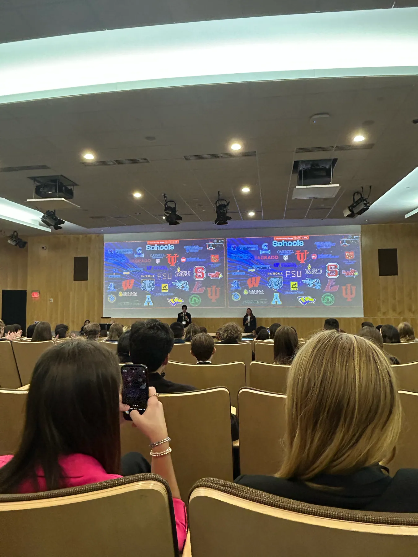 A Schools slide with dozens of university logos on the auditorium screens.
